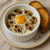 Œufs cocotte fondants à la crème et aux champignons, cuits doucement au four, pour une texture veloutée et un goût boisé délicat.
