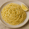Assiette de spaghettis crémeux au citron et parmesan, parsemée de zestes et d’herbes fraîches, servie avec un quartier de citron.