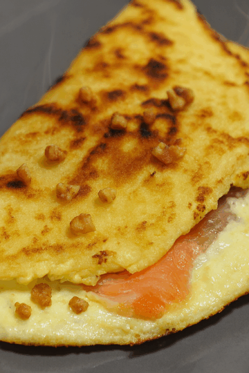 Brique au saumon garnie de crème fraîche et de petits éclats de noix, servie chaude avec un léger filet de fumée sur une assiette grise.