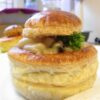 Vol-au-vent feuilleté doré, garni d’une crème onctueuse aux champignons. Le chapeau du feuilleté est légèrement posé de travers, laissant apparaître la garniture crémeuse et un brin de persil frais.